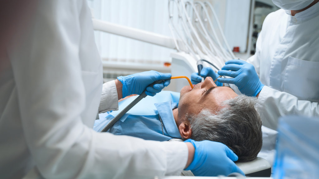 Dentist and his assistant are treating man in dental chair and giving him root canal treatment