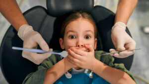 Little girl covering her mouth in the dental chair while trying to overcome dental anxiety.