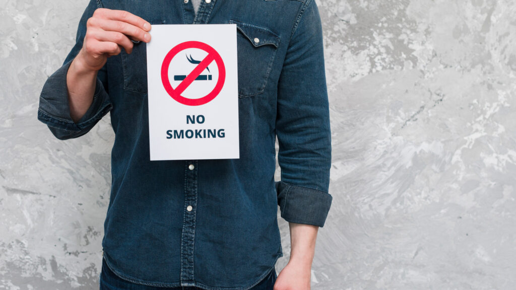 Image of man holding a no smoking sign to represent smoking and oral health and the negative aspects of it.