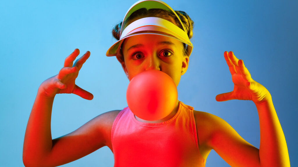 Young girl blowing a bubble of sugar-free gum after hearing about it as a 
travel tip for good oral health.