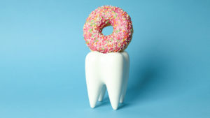 Does sugar really hurt your teeth? Image of a tooth with a pink donut on top of it.