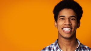 Image of young boy smiling against yellow background showing confidence and why straight teeth matter.