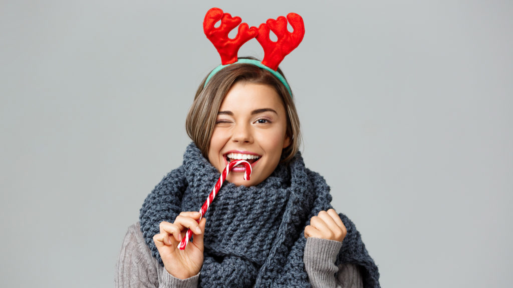 Girl wearing toy antlers and biting a candy cane thinking about New Year's Resolutions for your teeth.
