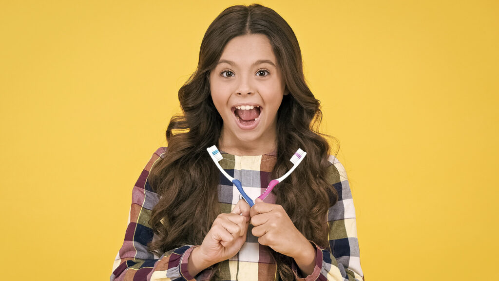 Young girl with an excited face holding two toothbrushes after she asked When should I get a new toothbrush?
